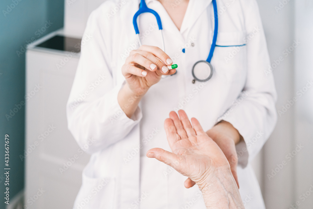 Cropped unrecognizable female medic in uniform and disposable mask preparing medications for anonymous elderly patient during consultation in clinic Cropped unrecognizable female medic in uniform and disposable mask preparing medications for anonymous elderly patient during consultation in clinic