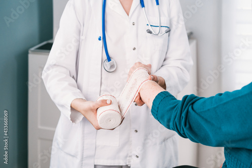 Crop anonymous doctor in uniform wrapping gauze around wrist of patient in hospital