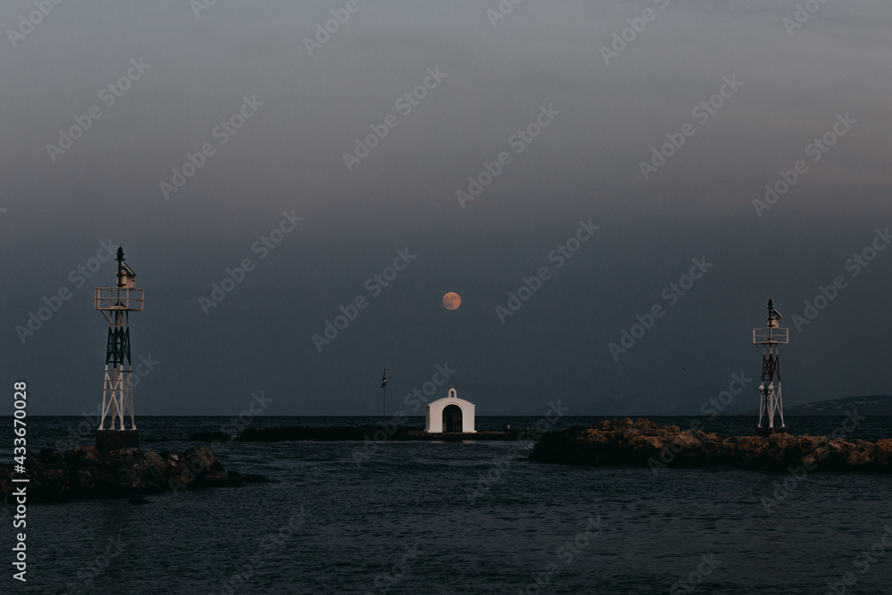 Scenic view of small white St Nickolas Church located on islet under dark sky with luminous moon at dusk Scenic view of small white St Nickolas Church located on islet under dark sky with luminous moon at dusk