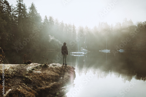 Anonymous person standing looking at a lake on a foggy day