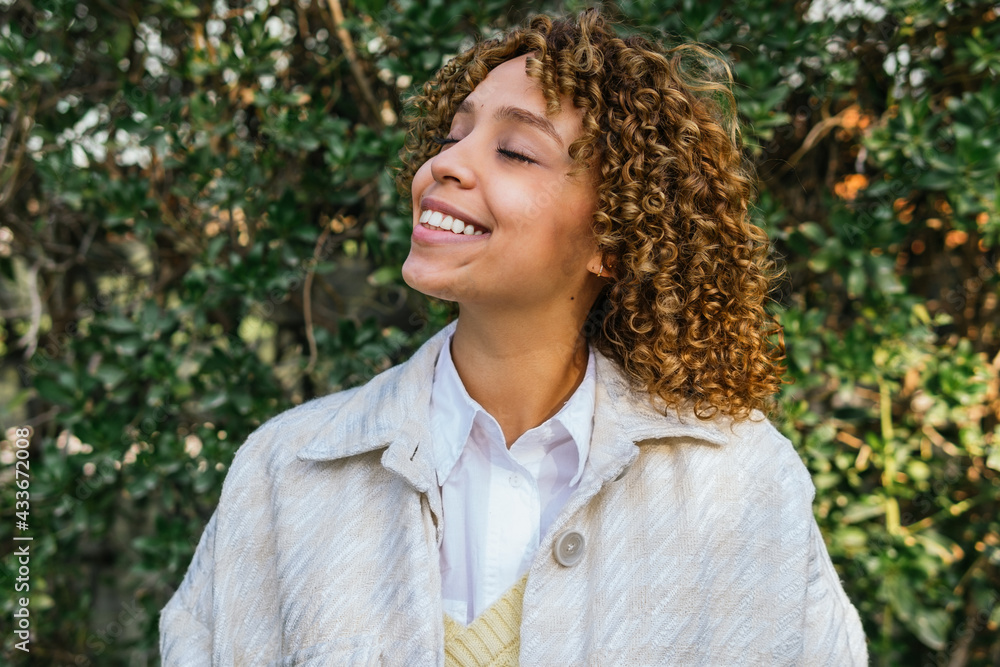 Dreamy African American female standing with closed eyes in green summer park and enjoying nature Dreamy African American female standing with closed eyes in green summer park and enjoying nature