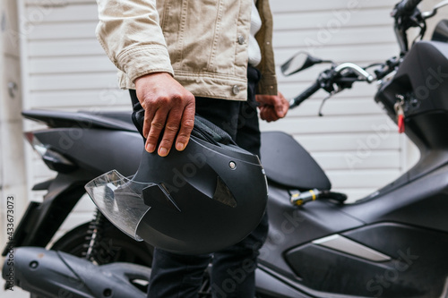 Side view of crop anonymous male motorcyclist with protective helmet standing against modern motorbike in town photo