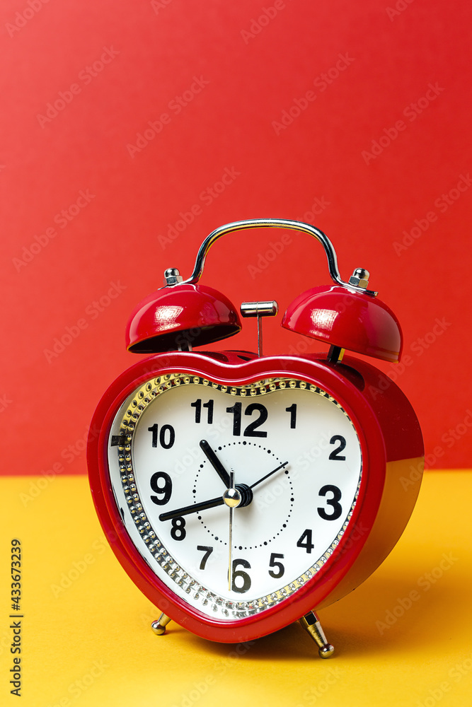 Red metal alarm clock in shape of heart placed on vibrant two colored background in studio Red metal alarm clock in shape of heart placed on vibrant two colored background in studio