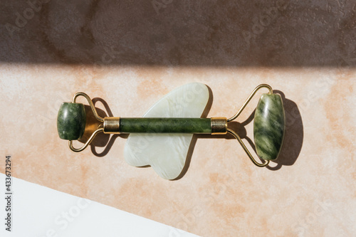 Top view of jade roller and guasha scraper arranged on marble table for concept of face massage