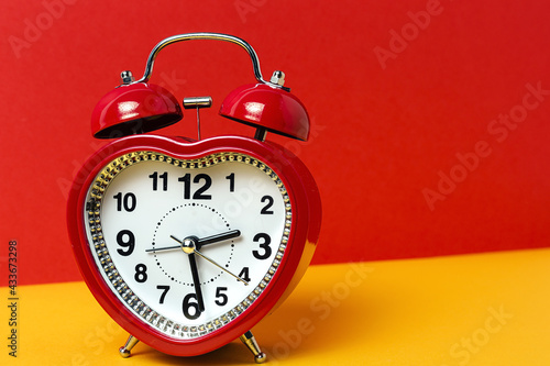 Red metal alarm clock in shape of heart placed on vibrant two colored background in studio photo
