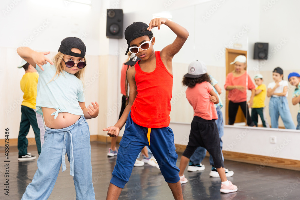 Portrait of confident preteen white girl and afro boy breakdancers in dance studio with dancing children in background..