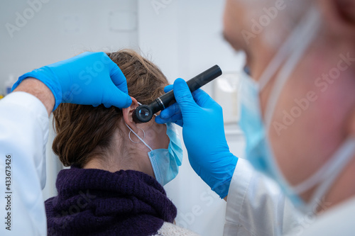 Male otolaryngologist in mask and gloves checking ears of patient with otoscope during appointment in hospital