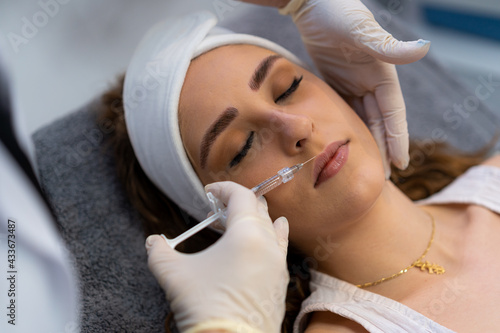 From above of crop unrecognizable professional beautician with syringe injecting filler with hyaluronic acid in lips of female client during procedure in beauty clinic photo