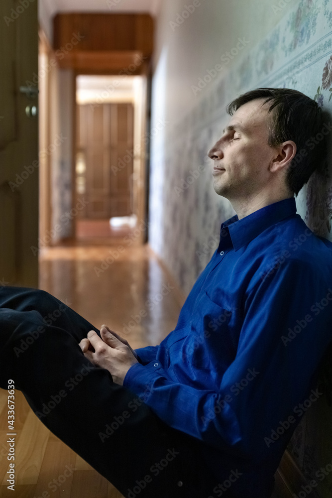 A young tired man is sitting on the floor in the corridor. Blue light A young tired man is sitting on the floor in the corridor. Blue light