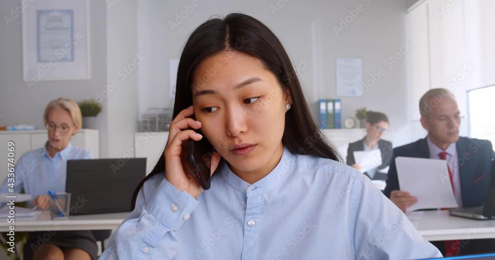 Asian young woman sitting at desk working and answering phone call Asian young woman sitting at desk working and answering phone call
