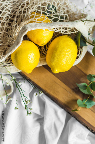 Colorful whole lemons in zero waste bag near wavy plant sprig on wooden chopping board on creased textile