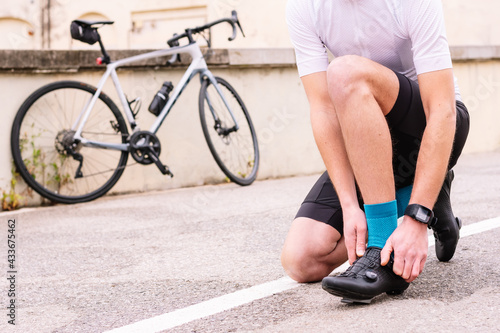 Crop unrecognizable male bicyclist in sports clothes and modern cycling shoes squatting on roadway against bike