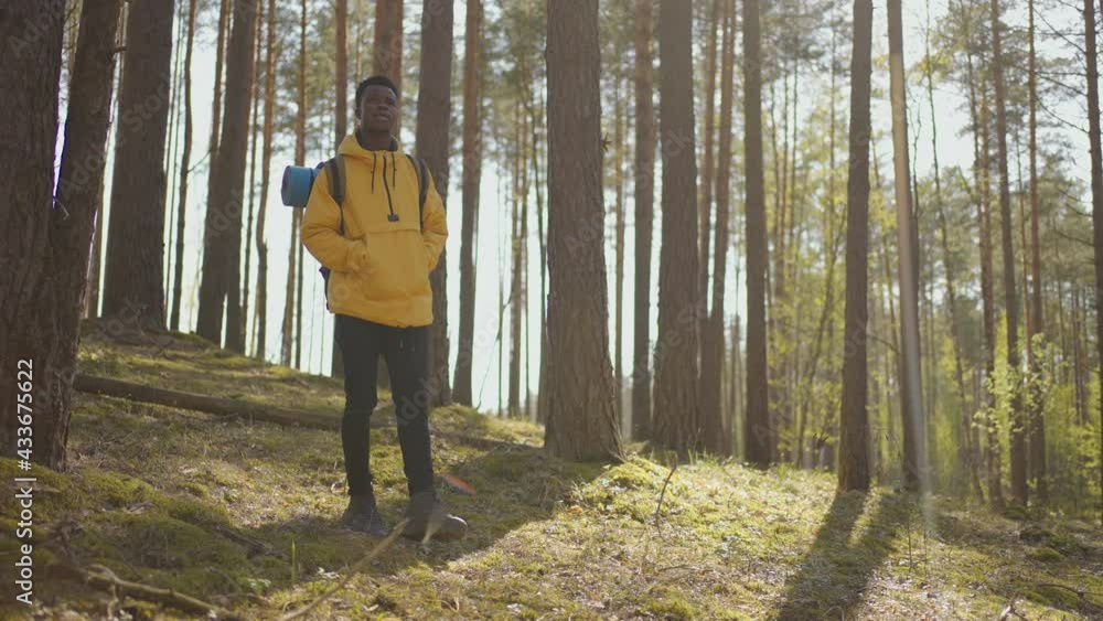 African black man climbs uphill in woods in yellow jacket with backpack in slow motion African black man climbs uphill in woods in yellow jacket with backpack in slow motion