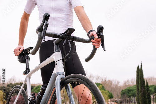 From below of masculine male cyclist in sportswear and bike looking away against cypress trees photo