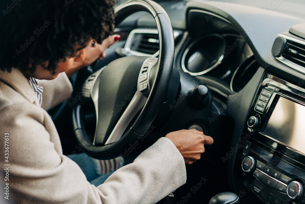 High angle of crop African American female driver starting auto engine with key sitting at steering wheel High angle of crop African American female driver starting auto engine with key sitting at steering wheel