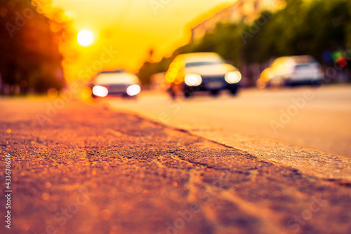 Sunset in the city, the cars driving on the road. Close up view from the sidewalk level