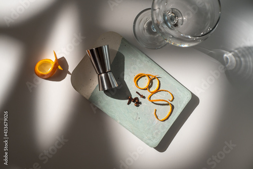 From above of glass near metal jigger with citrus fruit zest and dry condiments on table with shadows photo