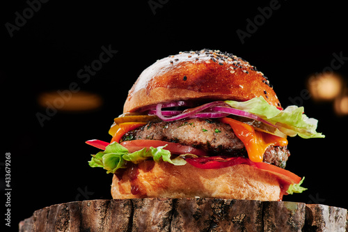 Beef burger with cheese, tomatoes, red onions, cucumber and lettuce on wooden cut on black background. Burger menu. Space for text. Unhealthy food. High quality photo