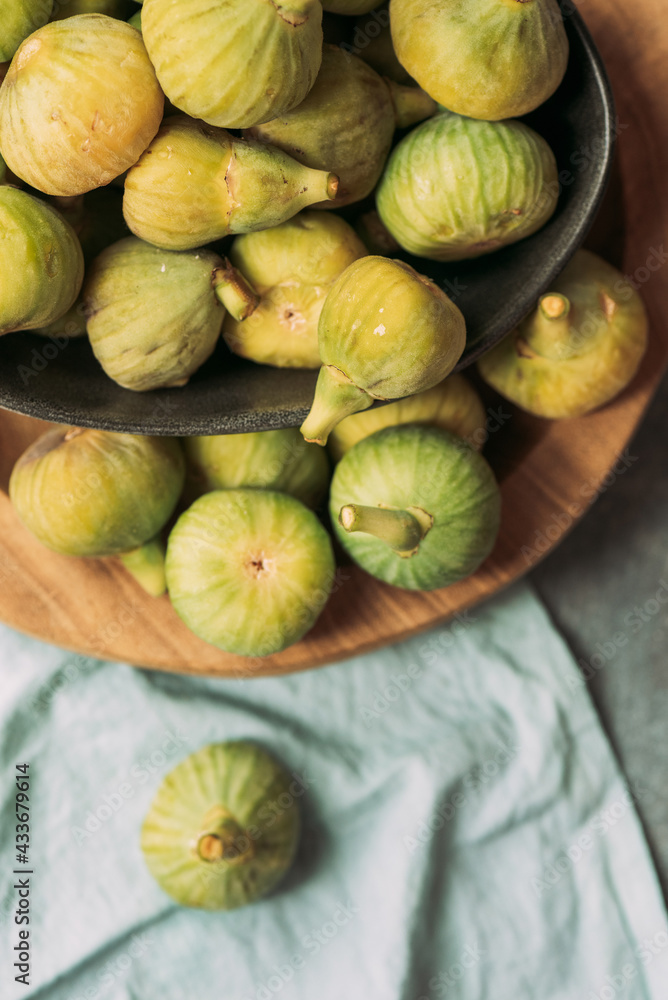 Fresh and ripe sweet green figs, in a black bowl on the wood plate served on the blue tablecloth table, Seasonal organic fruit. Also known as ripe white figs Fresh and ripe sweet green figs, in a black bowl on the wood plate served on the blue tablecloth table, Seasonal organic fruit. Also known as ripe white figs