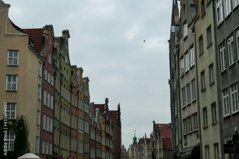 A deserted street in Old Town of Gdansk, Poland. The both sides of a paved alley have tall medieval buildings with colorful facades. Bell tower at the end of the alley. A bit of overcast. City tour.