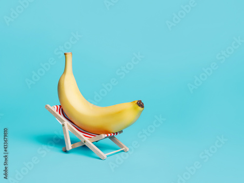 Billede på lærred Yellow fresh banana laying on a deck chair on vibrant blue background