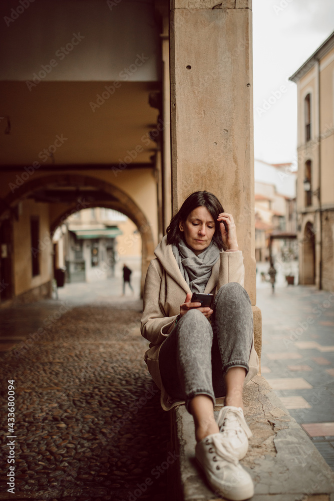Front view of female in outerwear text messaging on cellphone while touching face in city Front view of female in outerwear text messaging on cellphone while touching face in city
