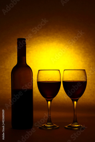 Silhouette of a red wine bottle and wine glasses with a yellow sunlight sunset type light burst