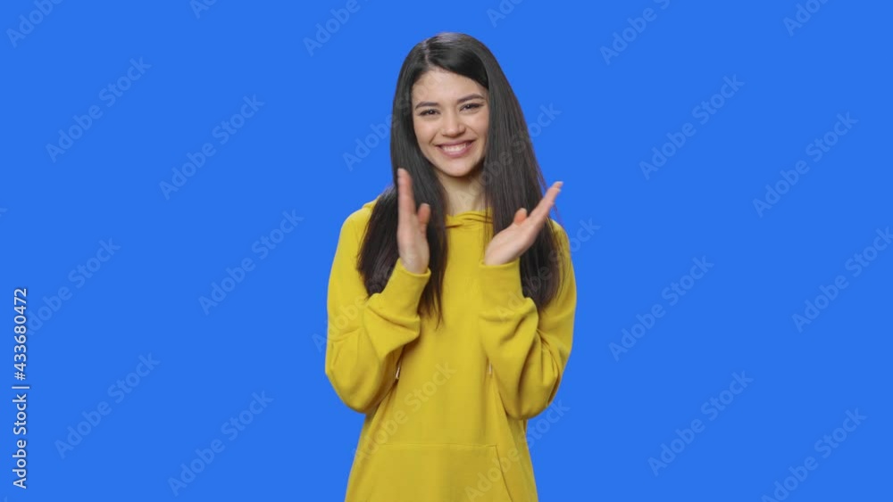 Portrait of pretty brunette clapping her hands happily. Young woman with long hair in yellow sweatshirt posing in studio with blue screen background. Close up. Slow motion ready 59.94fps. Portrait of pretty brunette clapping her hands happily. Young woman with long hair in yellow sweatshirt posing in studio with blue screen background. Close up. Slow motion ready 59.94fps.