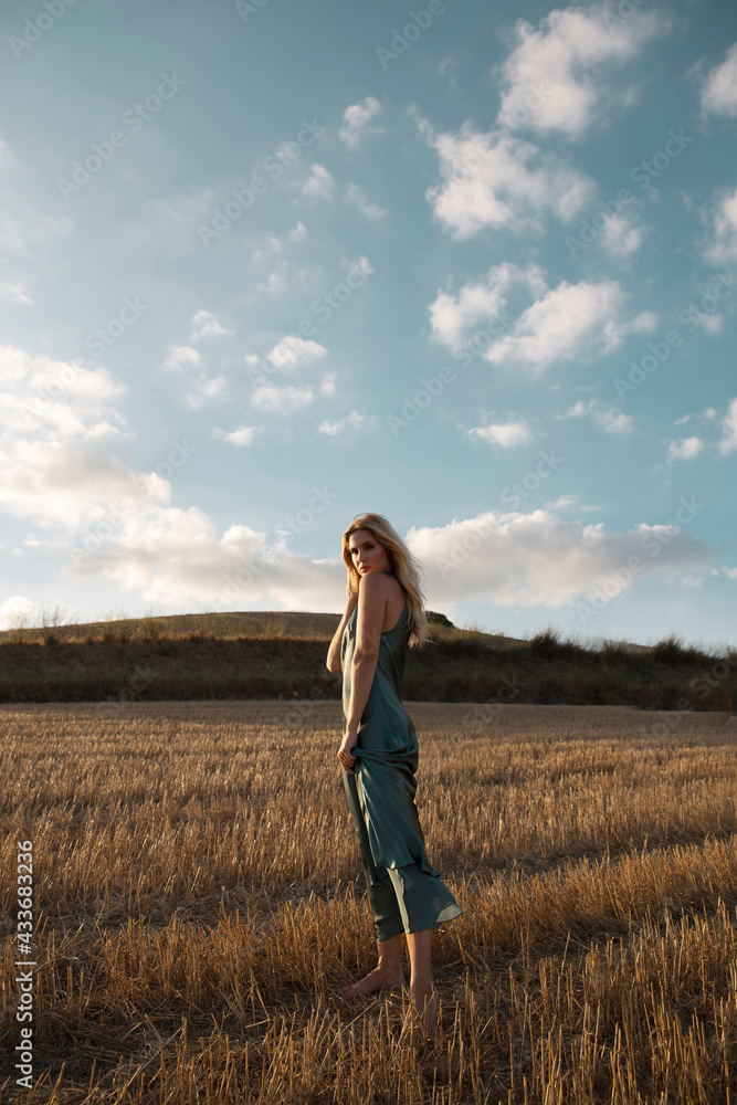 Peaceful female in elegant dress standing on dry field in rural area and looking at camera Peaceful female in elegant dress standing on dry field in rural area and looking at camera