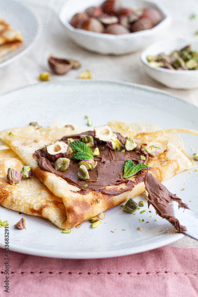 Delicious crepes garnished with chocolate and nuts served on plate on table for breakfast Delicious crepes garnished with chocolate and nuts served on plate on table for breakfast