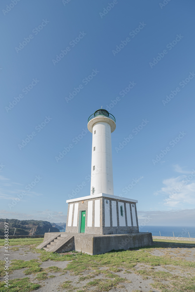 Asphalt road leading to white lighthouse placed in Faro de Lastres in Asturias in Spain under cloudless blue sky in daytime Asphalt road leading to white lighthouse placed in Faro de Lastres in Asturias in Spain under cloudless blue sky in daytime