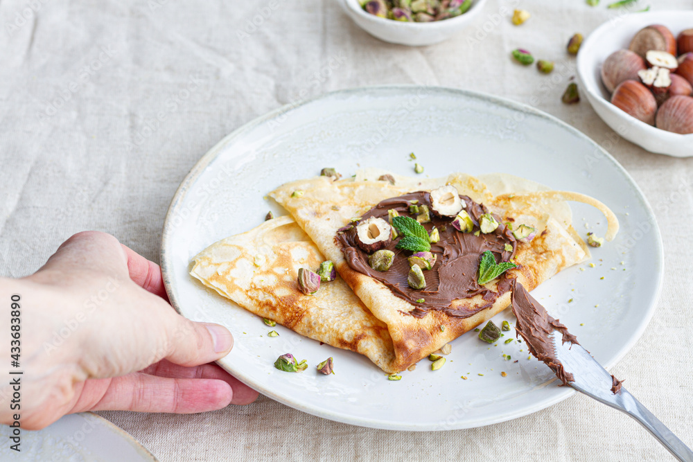 Cropped unrecognizable book holding plate with delicious crepes garnished with chocolate and nuts on table for breakfast Cropped unrecognizable book holding plate with delicious crepes garnished with chocolate and nuts on table for breakfast