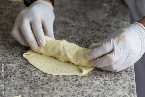 Chef wraps pizza ingredients in dough with his hands.