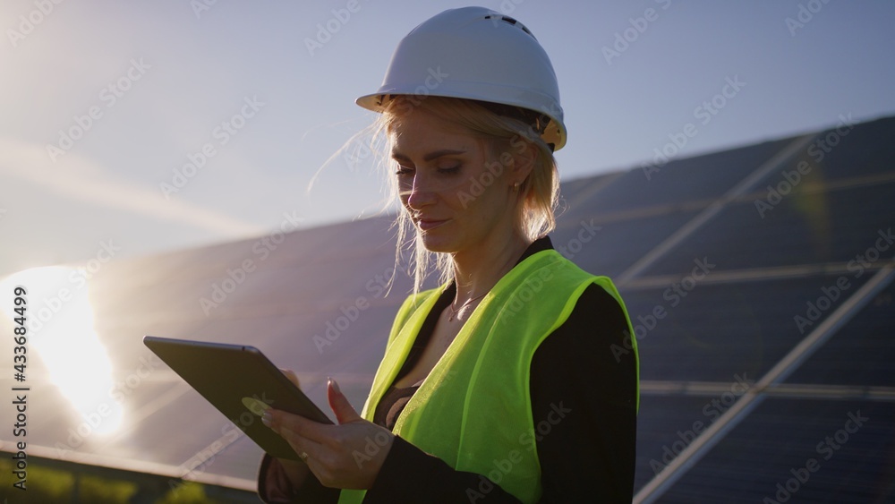 Portrait of a blonde female solar engineer standing uses a tablet and looking away Portrait of a blonde female solar engineer standing uses a tablet and looking away