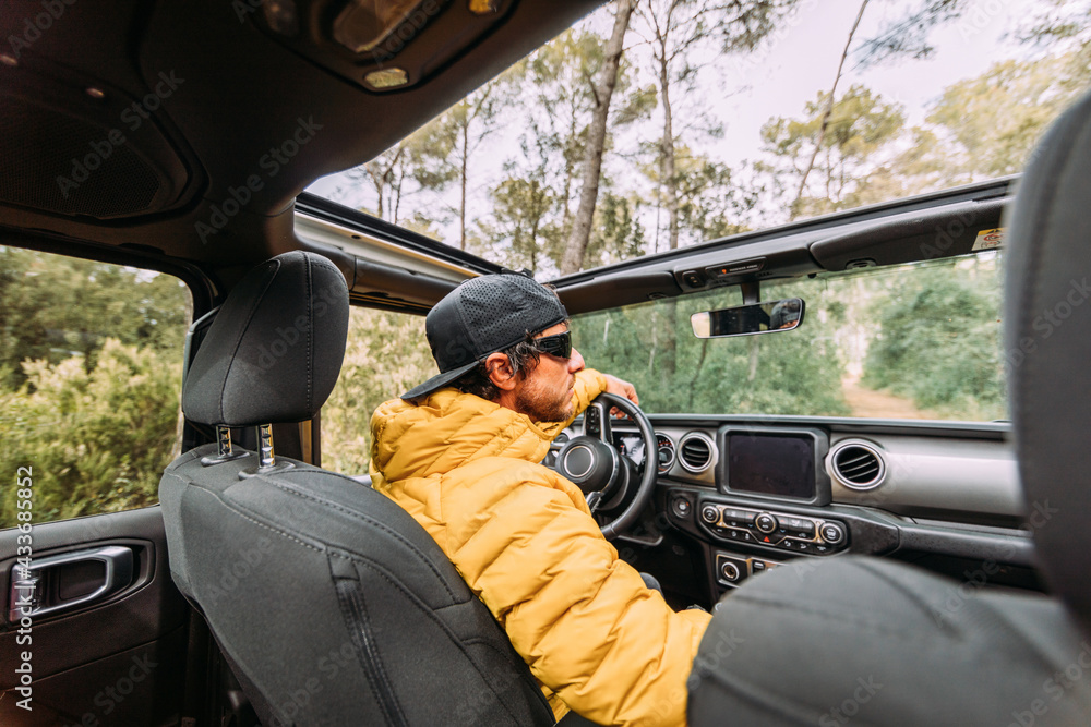 From behind inside view of a driver wearing a cap and sunglasses in an off-road car looking away From behind inside view of a driver wearing a cap and sunglasses in an off-road car looking away