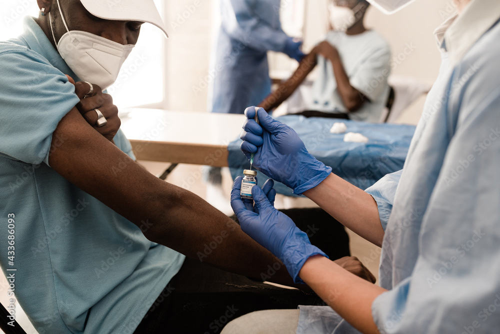 Crop hands of anonymous doctor in latex gloves filling in syringe from bottle with vaccine preparing to vaccinate unrecognizable male African American patient in clinic during coronavirus outbreak Crop hands of anonymous doctor in latex gloves filling in syringe from bottle with vaccine preparing to vaccinate unrecognizable male African American patient in clinic during coronavirus outbreak