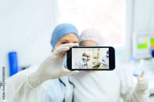 Anonymous female doctors in uniforms with thumb up taking self portrait on cellphone in hospital photo