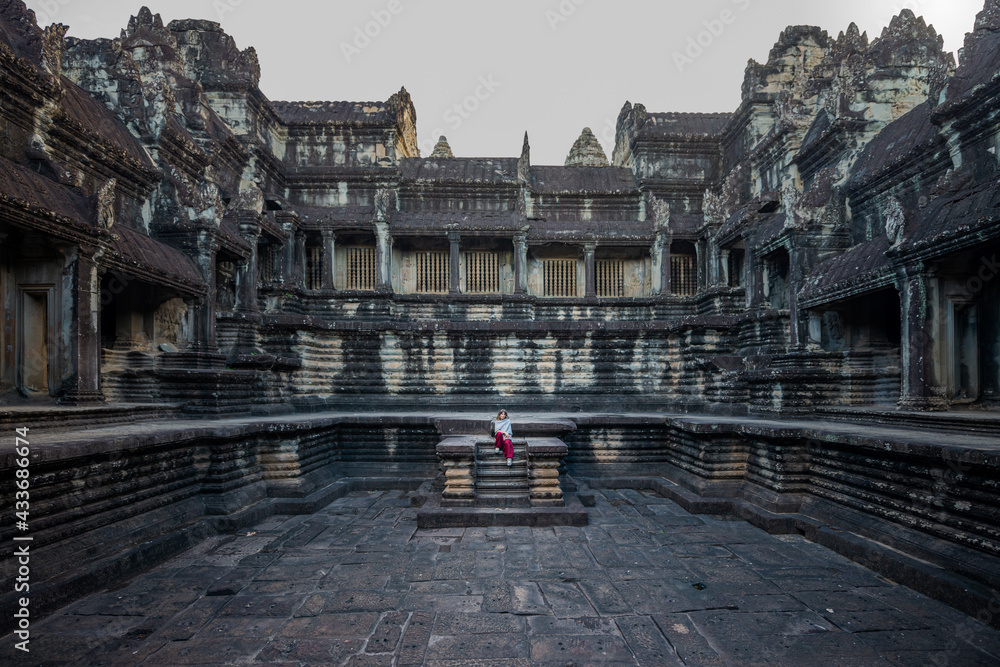 Anonymous female tourist on staircase against old oriental worship facade with colonnade during trip in Angkor Wat of Cambodia Anonymous female tourist on staircase against old oriental worship facade with colonnade during trip in Angkor Wat of Cambodia