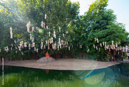 Buddha sculpture on stone under lanterns on trees against oriental construction reflecting in pure pond in Thailand