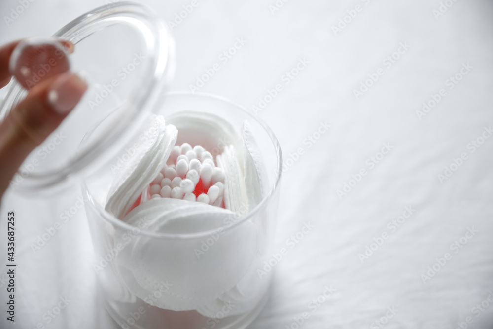 A hand opening clear container for cotton pads on a white background. A hand opening clear container for cotton pads on a white background.