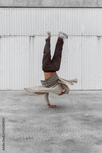 Unrecognizable male dancer showing breakdance movement while balancing on arms and performing Hand Hops on concrete ground in urban area