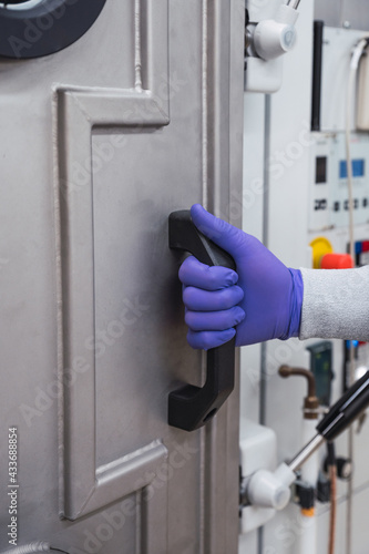 Crop faceless laboratory worker in protective latex gloves opening door of enclosed biosafety facility while working in modern equipped lab