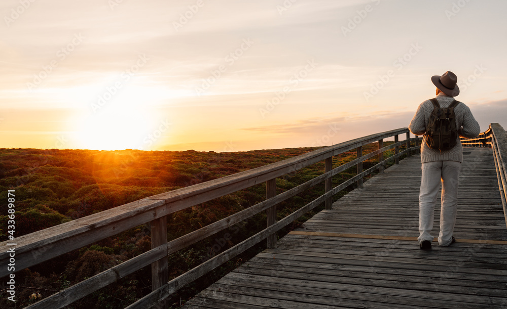 Man with backpack and hat walking on a walkway looking the horizon Man with backpack and hat walking on a walkway looking the horizon