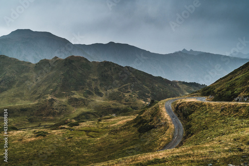 Picturesque landscape of empty route surrounded with dry and green grass in mountainous terrain of Aran Valley in Spain under gray cloudy sky
