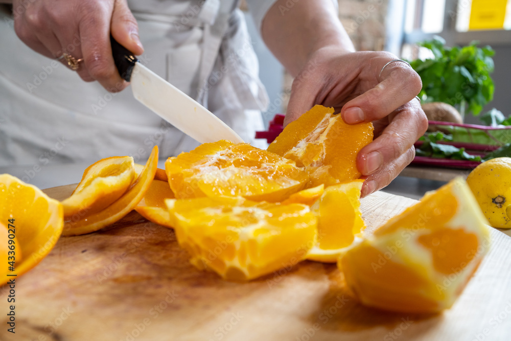 Crop unrecognizable female cutting ripe juicy oranges with knife on wooden chopping board at kitchen table Crop unrecognizable female cutting ripe juicy oranges with knife on wooden chopping board at kitchen table
