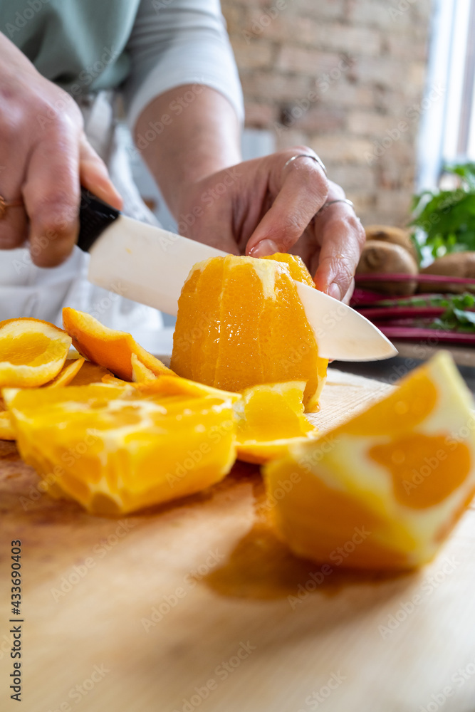 Crop unrecognizable female cutting ripe juicy oranges with knife on wooden chopping board at kitchen table Crop unrecognizable female cutting ripe juicy oranges with knife on wooden chopping board at kitchen table