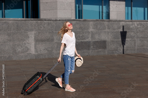 Happy blonde woman with suitcase goes summer in the sun