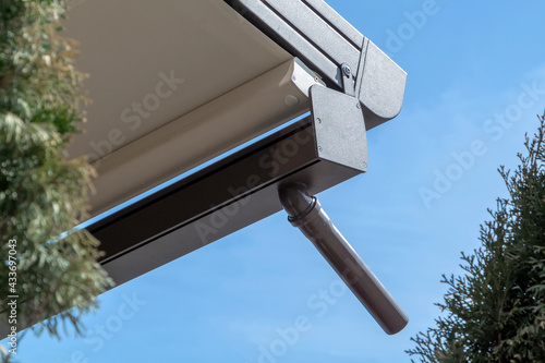 canvas awning with metal frame and drainage pipe against blue sunny sky. modern shading for house