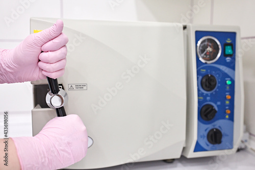 White autoclave in sterilization room in clinic. Hands in pink gloves closes the autoclave.Sterilization of instruments. Dentist tools. Sterilization procedure. Steam autoclave. 