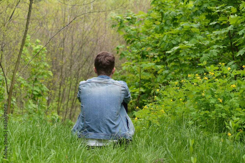 Obraz premium Young man sitting in spring forest, back view 